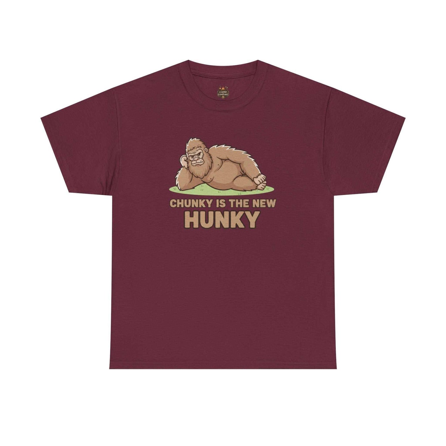 A man wearing the Chunky Is The New Hunky T-Shirt | Funny Bigfoot Sasquatch Tee while leaning against a rustic wooden fence in a mountain setting, showcasing the relaxed fit.