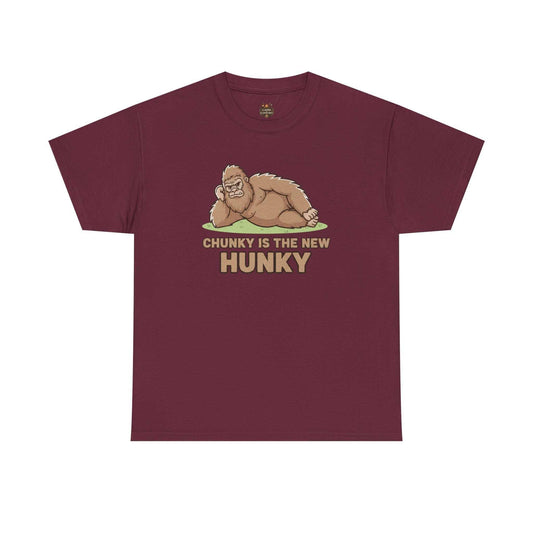 A man wearing the Chunky Is The New Hunky T-Shirt | Funny Bigfoot Sasquatch Tee while leaning against a rustic wooden fence in a mountain setting, showcasing the relaxed fit.