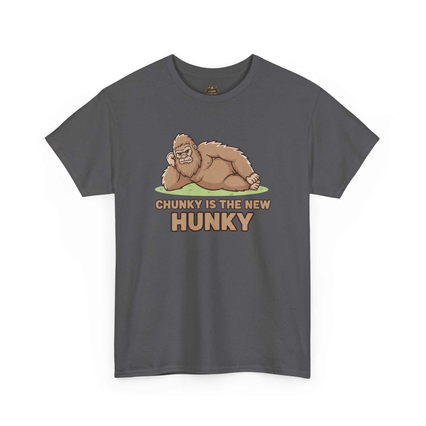 A man wearing the Chunky Is The New Hunky T-Shirt | Funny Bigfoot Sasquatch Tee while leaning against a rustic wooden fence in a mountain setting, showcasing the relaxed fit.
