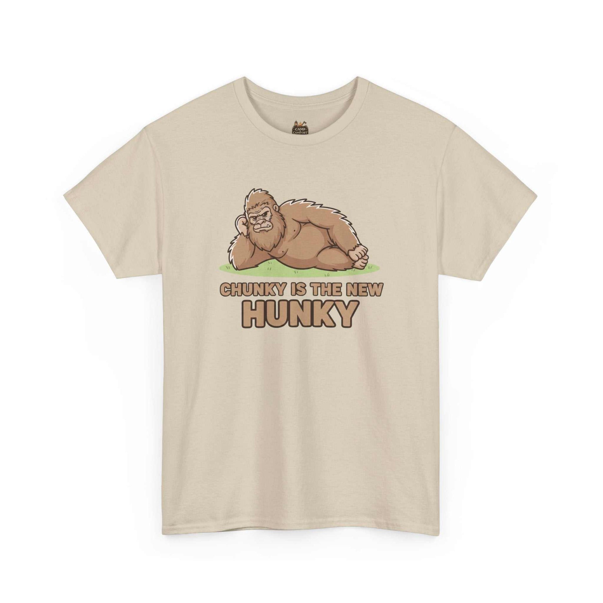 A man wearing the Chunky Is The New Hunky T-Shirt | Funny Bigfoot Sasquatch Tee while leaning against a rustic wooden fence in a mountain setting, showcasing the relaxed fit.