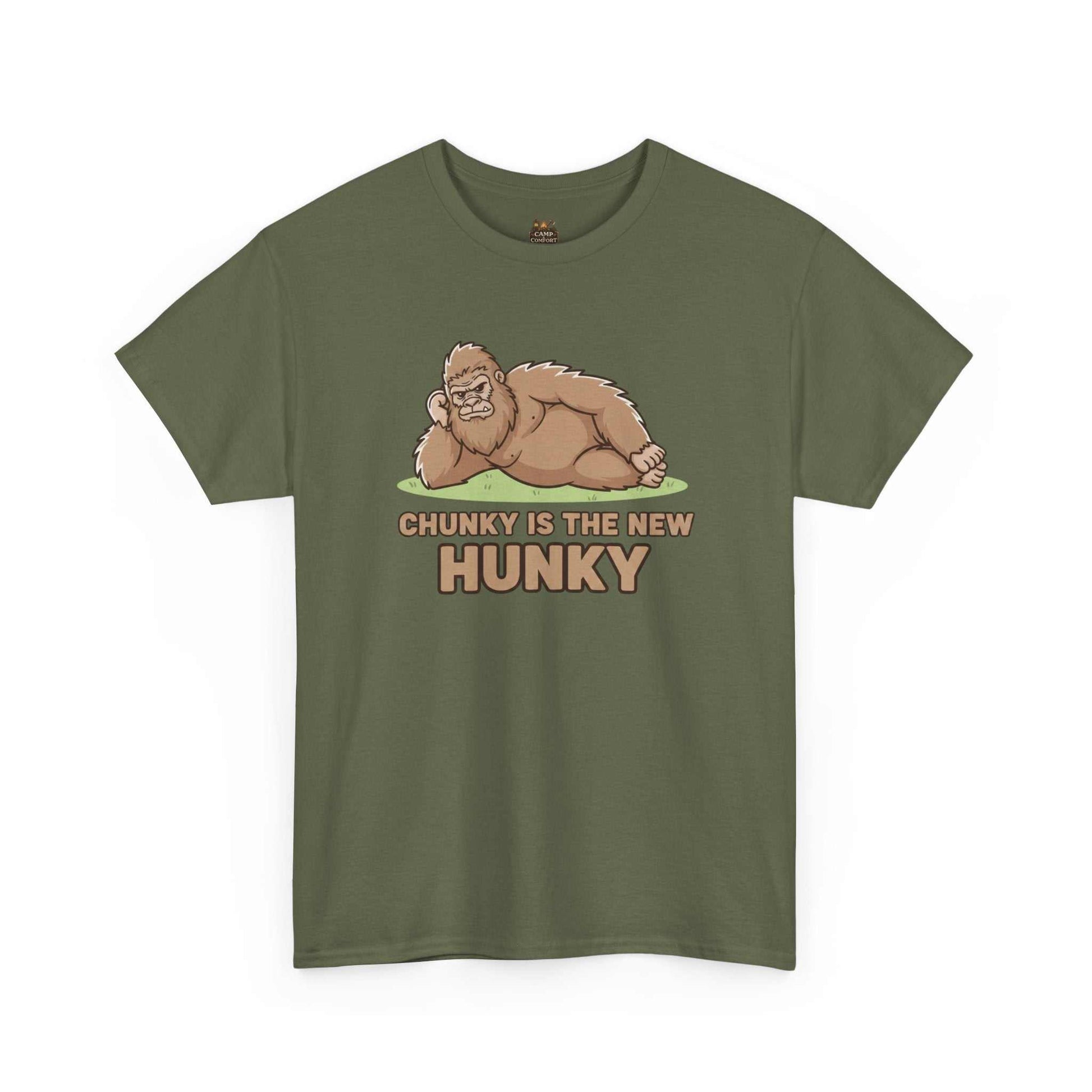 A man wearing the Chunky Is The New Hunky T-Shirt | Funny Bigfoot Sasquatch Tee while leaning against a rustic wooden fence in a mountain setting, showcasing the relaxed fit.