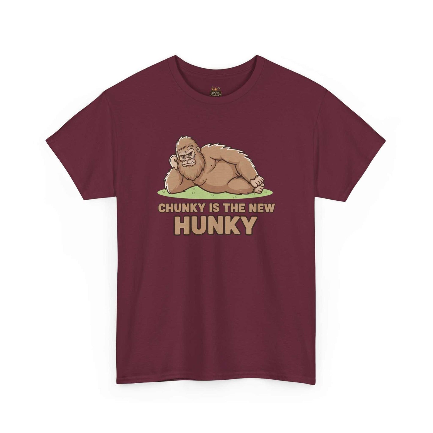 A man wearing the Chunky Is The New Hunky T-Shirt | Funny Bigfoot Sasquatch Tee while leaning against a rustic wooden fence in a mountain setting, showcasing the relaxed fit.